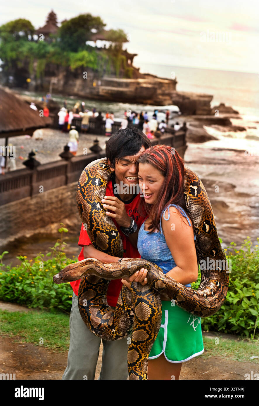 Un paio di turisti indonesiani posa per foto tenendo un grande python da Tanah Lot un antico tempio indù dal mare di Bali Foto Stock