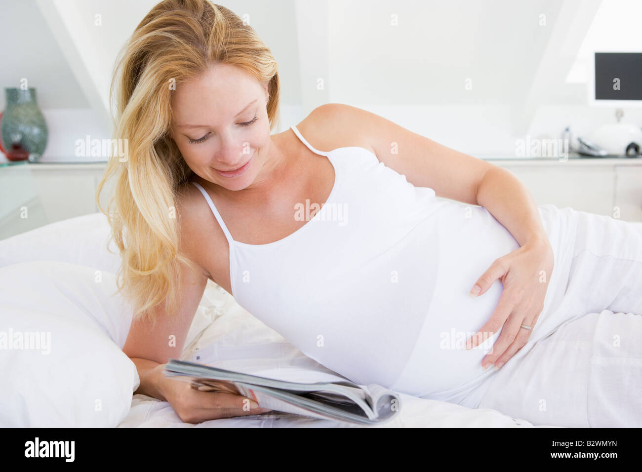 Donna incinta giacente in letto rivista lettura sorridente Foto Stock