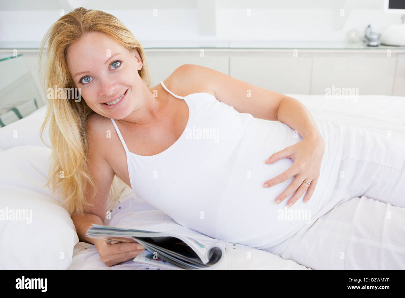 Donna incinta giacente in letto rivista lettura sorridente Foto Stock