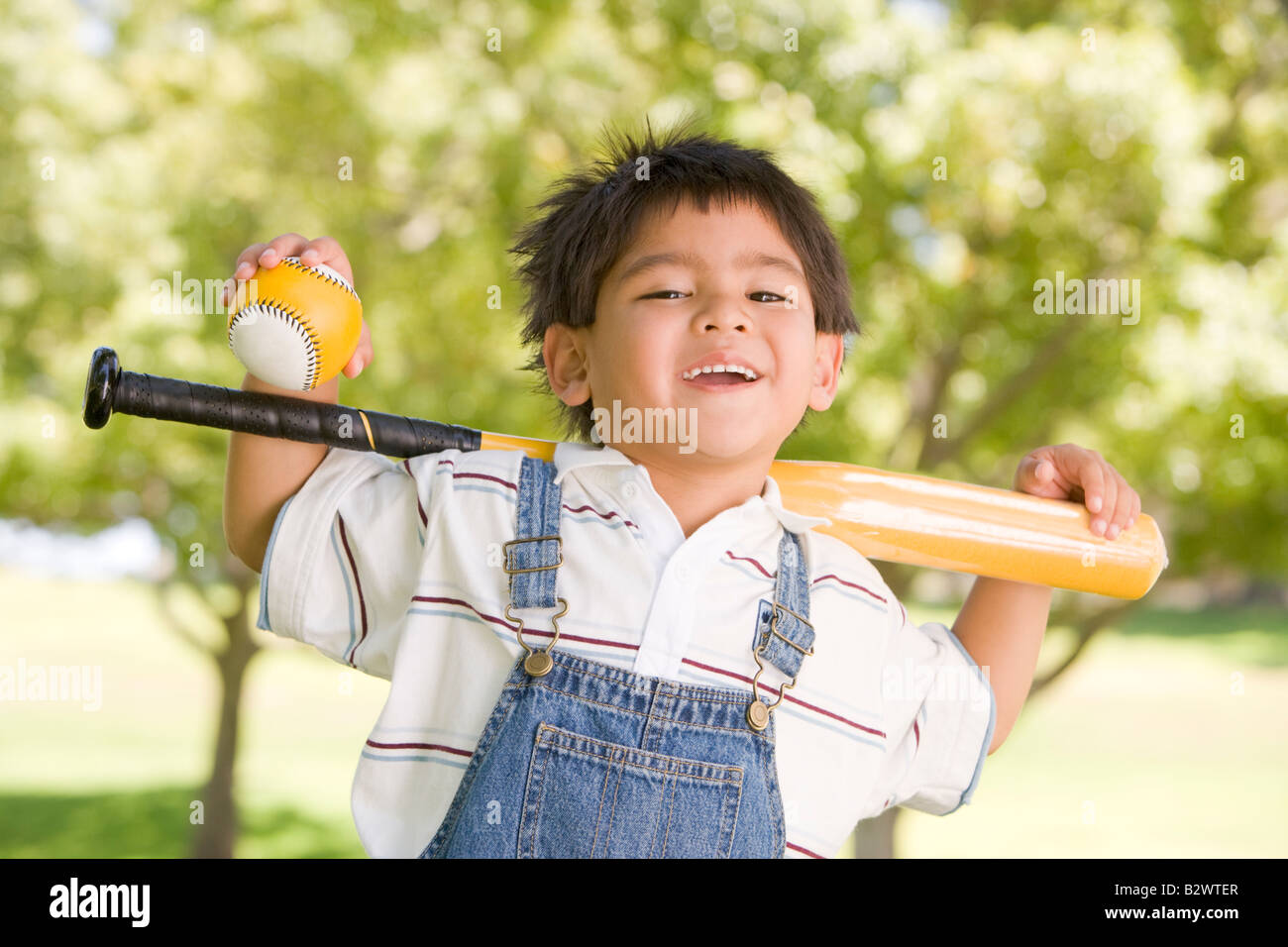 Ragazzo giovane azienda mazza da baseball all'aperto sorridente Foto Stock