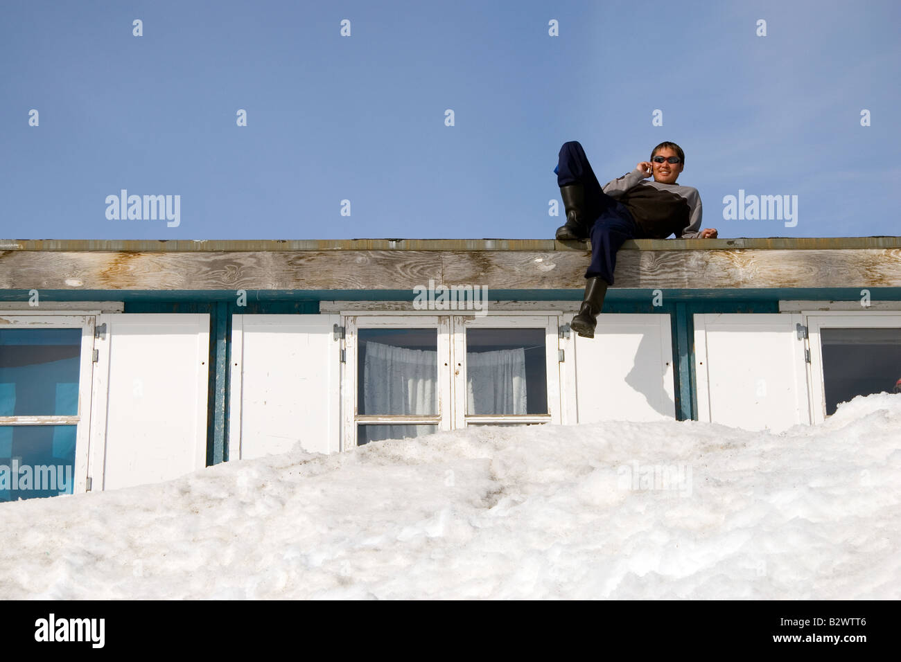 Un locale uomo Inuit utilizza il suo telefono cellulare dal tetto della sua casa nel villaggio di Ittoqqortoormiit, Scoresbysund, est della Groenlandia Foto Stock