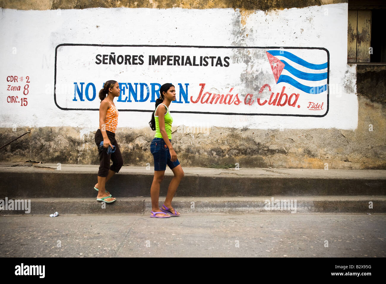 Due ragazze adolescenti a piedi da una pittura murale dicendo in spagnolo imperialisti sirs non sarai mai Cuba a Baracoa Cuba su Thursda Foto Stock