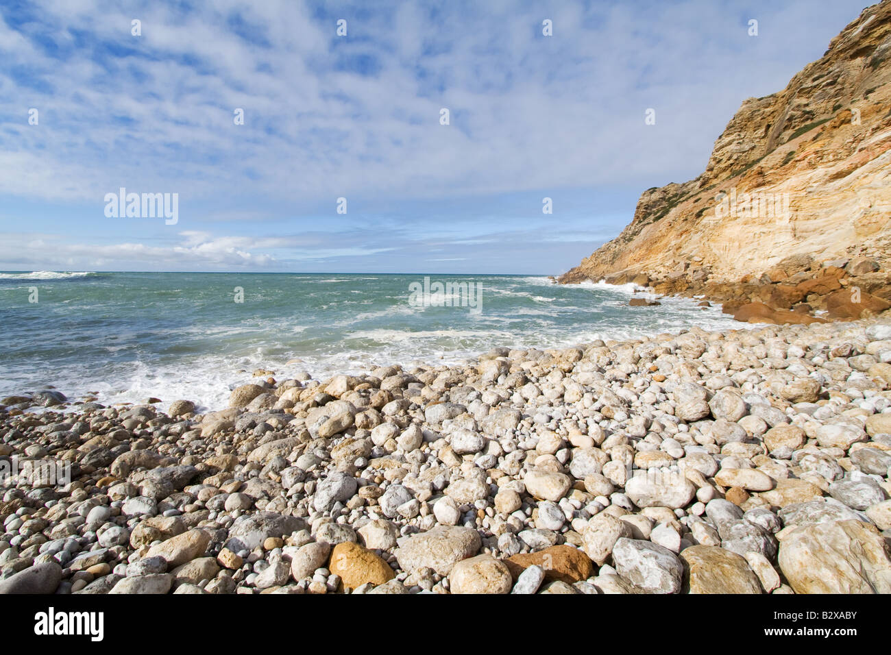 Spiaggia coperta di round di pietre e ciottoli a Cabo Espichel Cape, Sesimbra, Portogallo. pietra rocciosa sassoso pebble cove bay rocce della costa Foto Stock