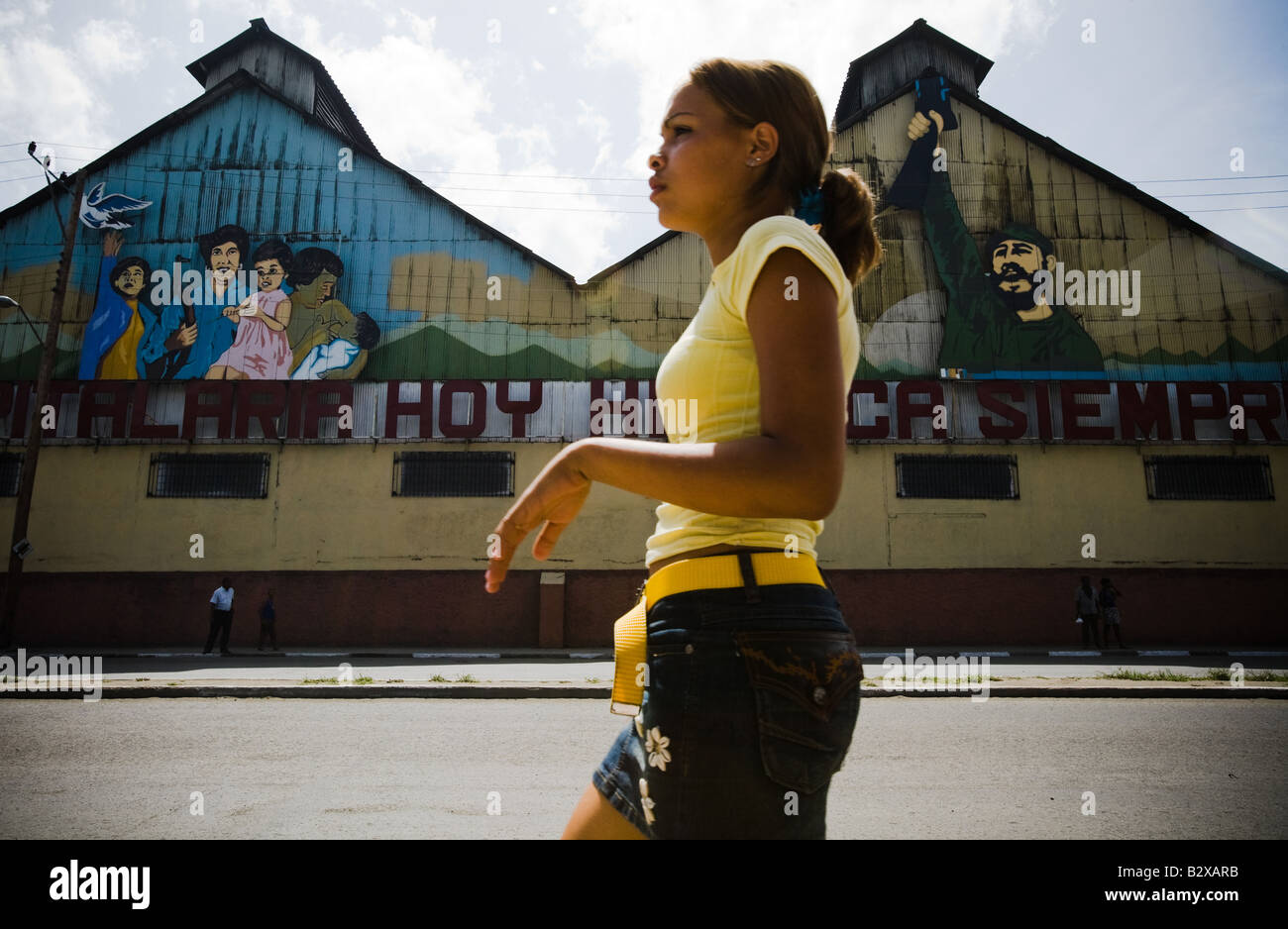 Una ragazza cammina passato un murale raffigurante Fidel Castro e una famiglia cubana di Santiago di Cuba - Foto Stock
