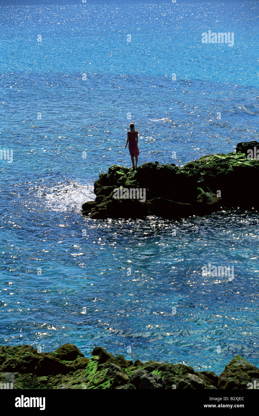 Donna all'aperto in piedi su grandi rocce Oceanside (lontano) Foto Stock