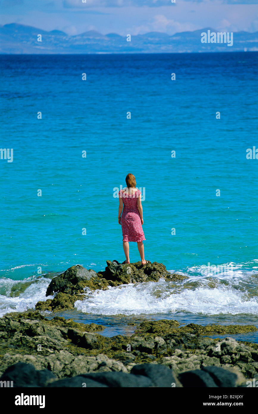 Donna all'aperto in piedi su rocce di grandi dimensioni mediante l'oceano Foto Stock