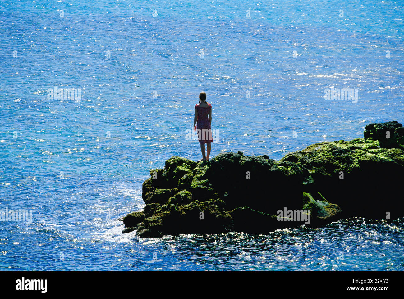 Donna all'aperto in piedi su rocce di grandi dimensioni mediante l'oceano Foto Stock