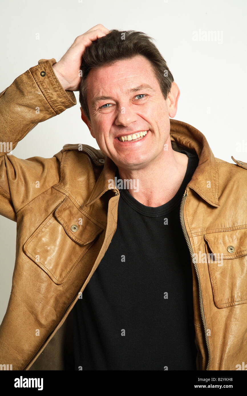 L uomo nella sua 40s sorridente indossa una giacca di pelle - la mano sulla testa Foto Stock