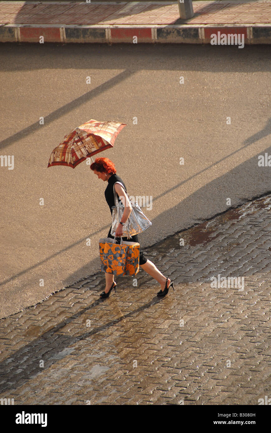 Donna attraversare una strada incrocio con un ombrello dopo una doccia Foto Stock