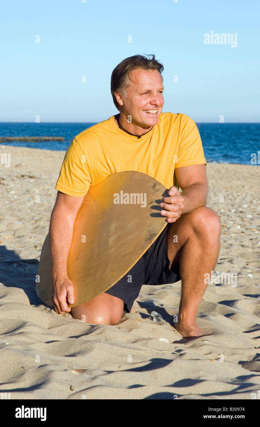 Una bella e felice degli anni quaranta uomo avendo divertimento sulla spiaggia e portando la sua tavola da surf. Foto Stock