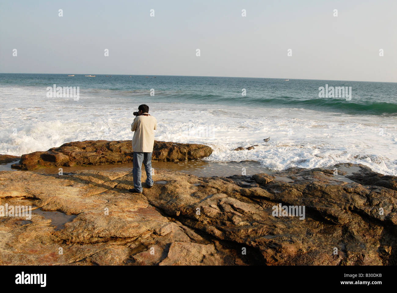 Una persona di scattare una foto della spiaggia rocciosa di Kovalam,Kerala, India Foto Stock