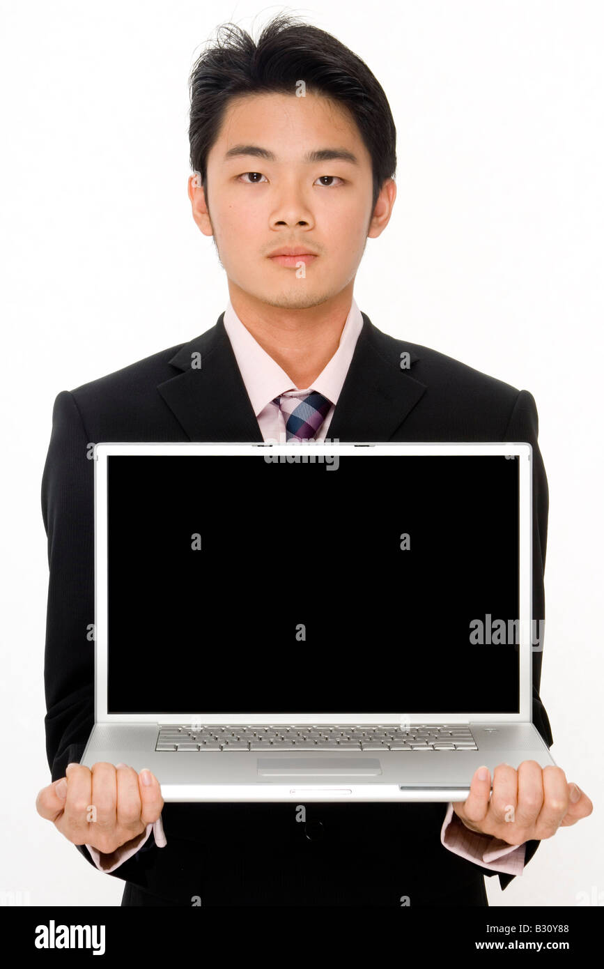 Un grave Asian businessman in possesso di un computer portatile con schermo nero Foto Stock