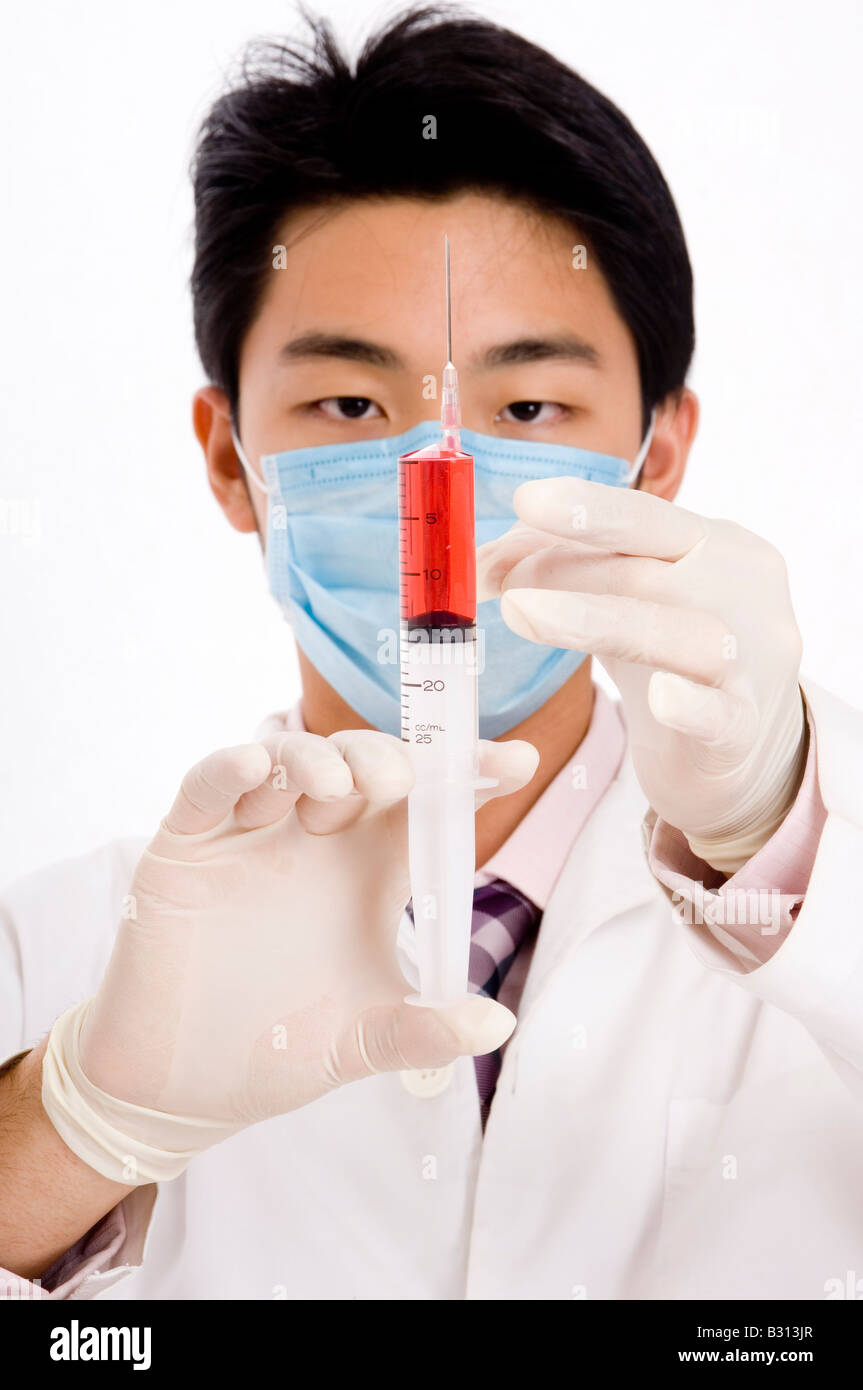 Un giovane maschio tecnico di laboratorio in maschera facciale e guanti in lattice tenendo una siringa Foto Stock