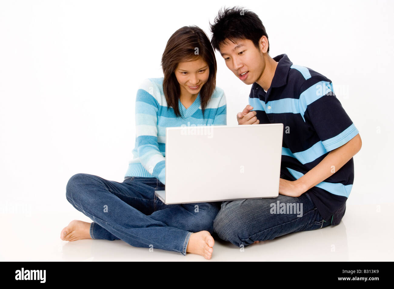Una giovane coppia seduta sul pavimento usando un computer portatile Foto Stock