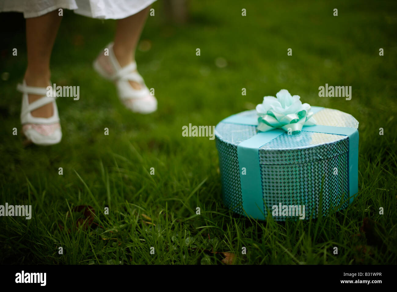 Bambina di cinque anni con scatola verde avvolto in nastro e rose, salti in aria i piedi da terra Foto Stock