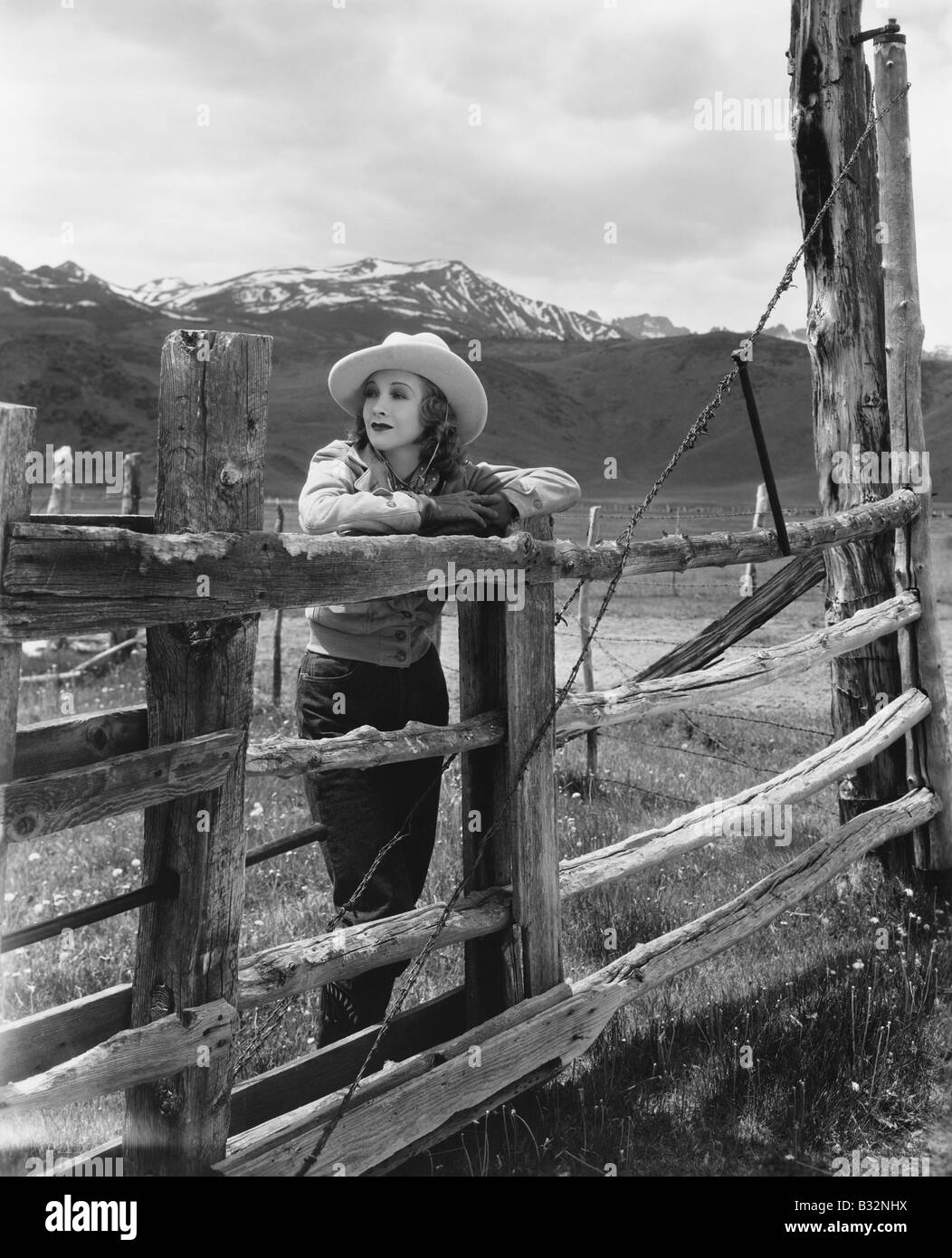 Donna appoggiata sulla staccionata in legno sul ranch Foto Stock