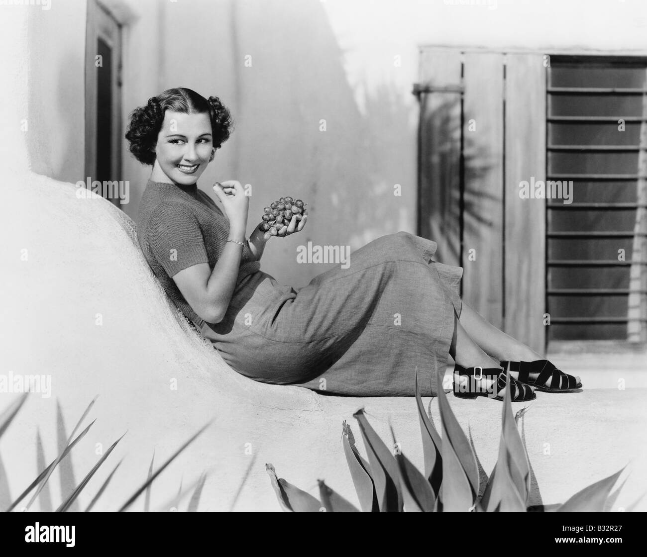 Giovane donna seduta sulla terrazza sorridente mangiare uva Foto Stock
