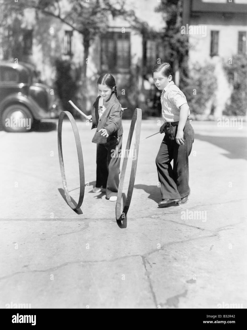 Un ragazzo e una ragazza giocando hoop e stick su un marciapiede Foto Stock