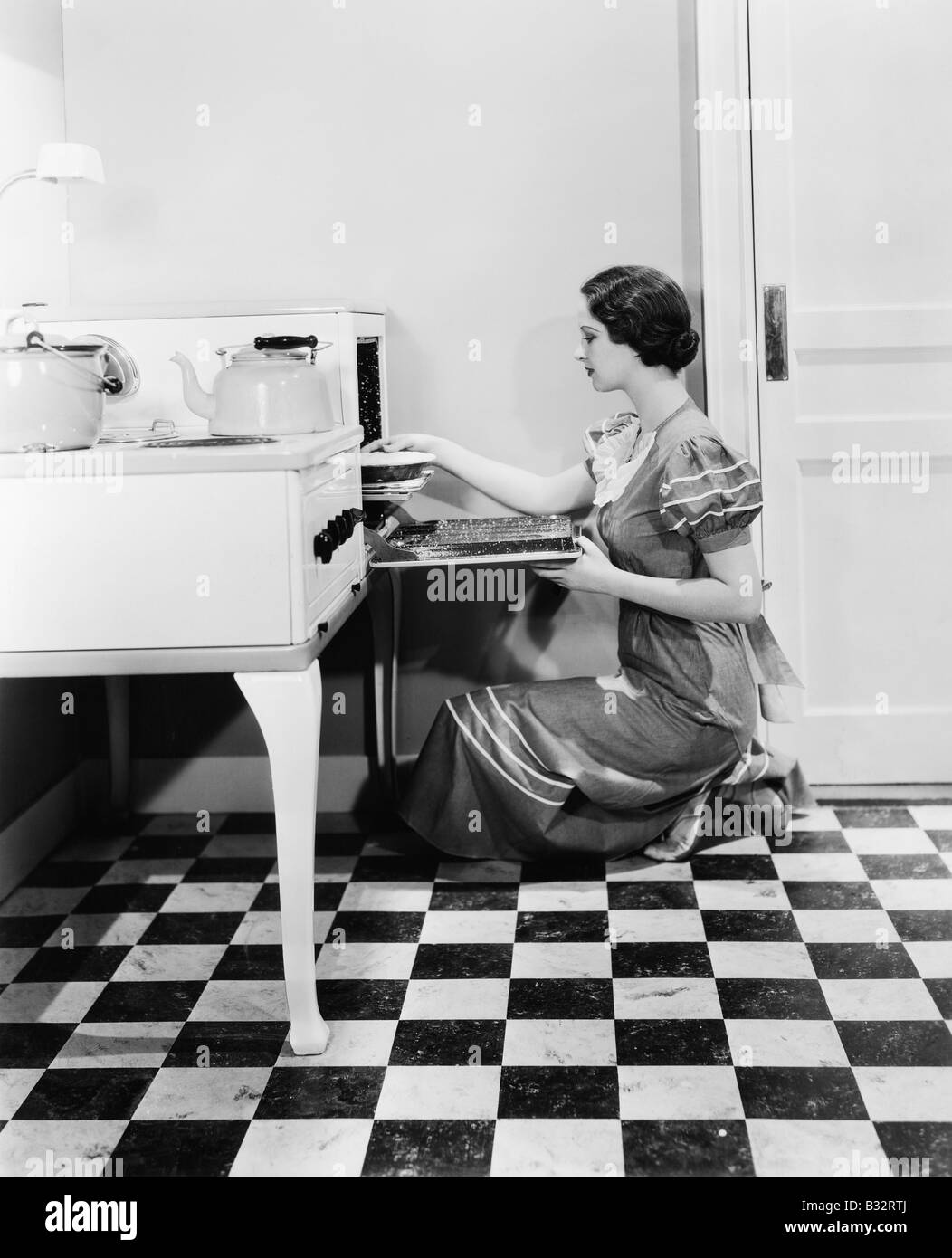 Profilo di una giovane donna mettendo una torta in un forno Foto Stock