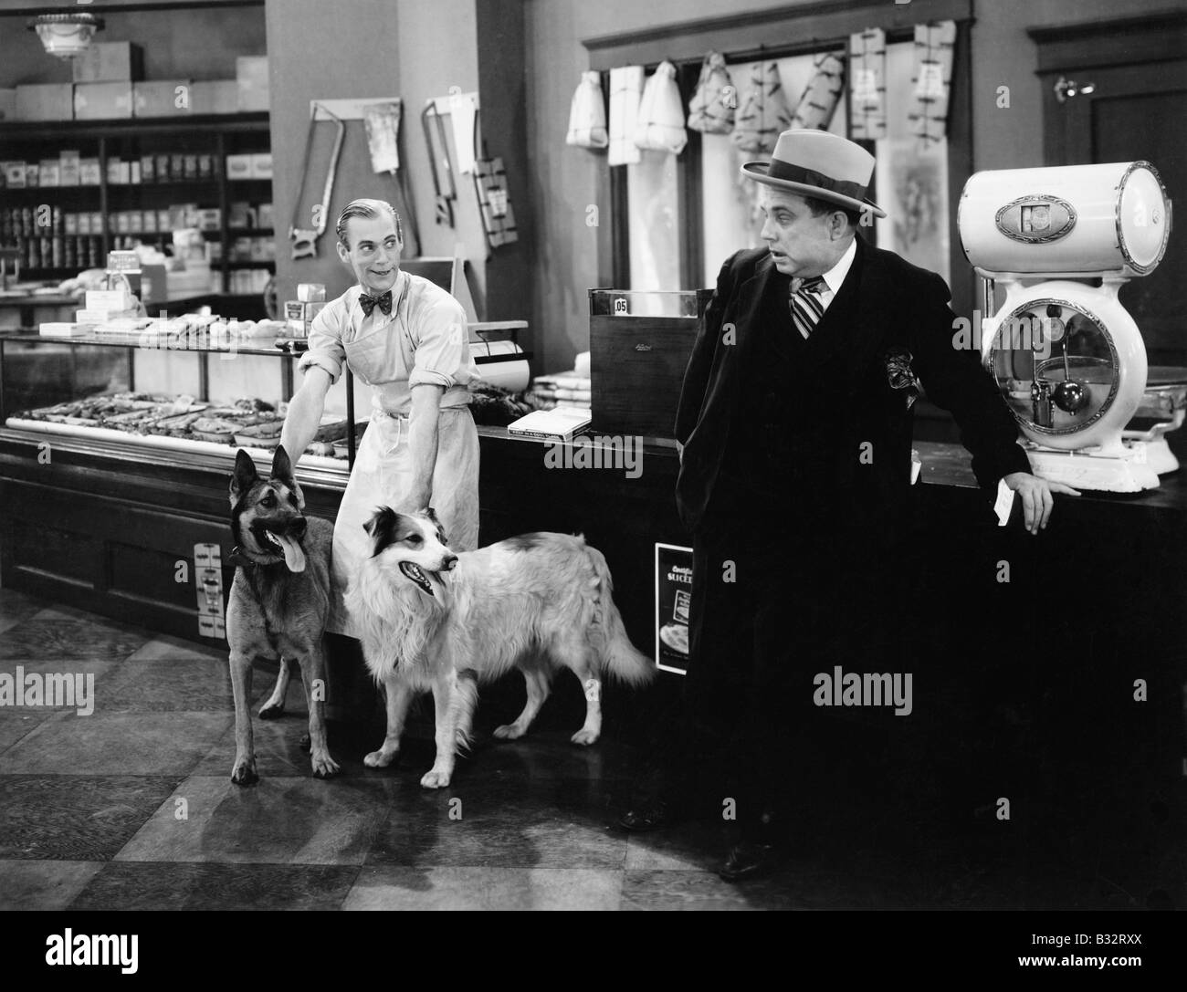 Uomo che guarda timoroso a due cani in un negozio di macellaio Foto Stock