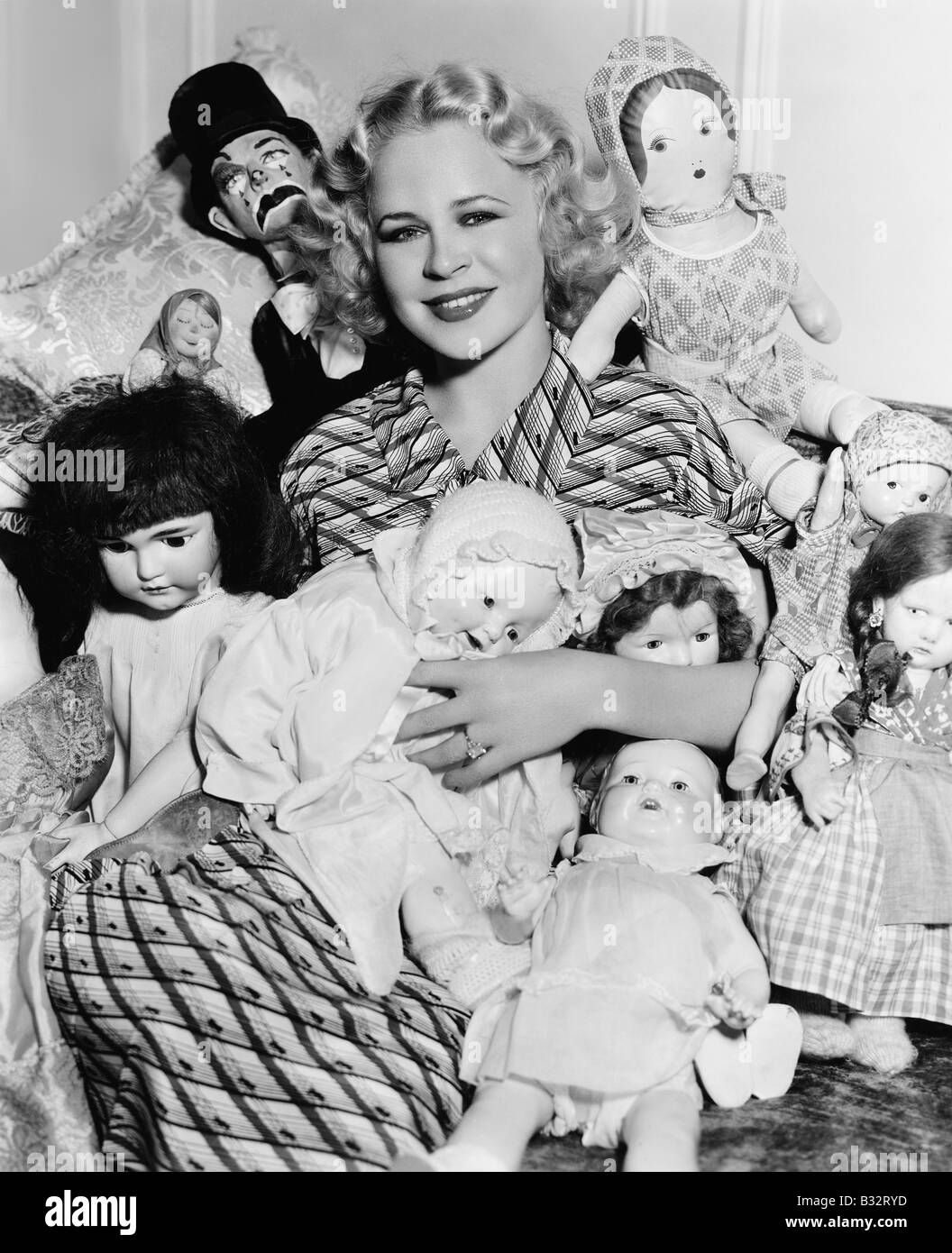 Ritratto di donna circondata da bambole e sorridente Foto Stock
