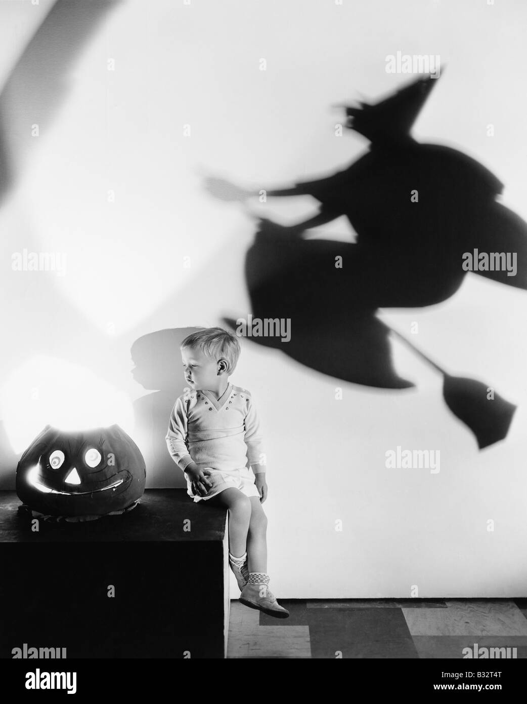 Ragazzo seduto su una tabella con una zucca e un'ombra di una strega su una parete Foto Stock