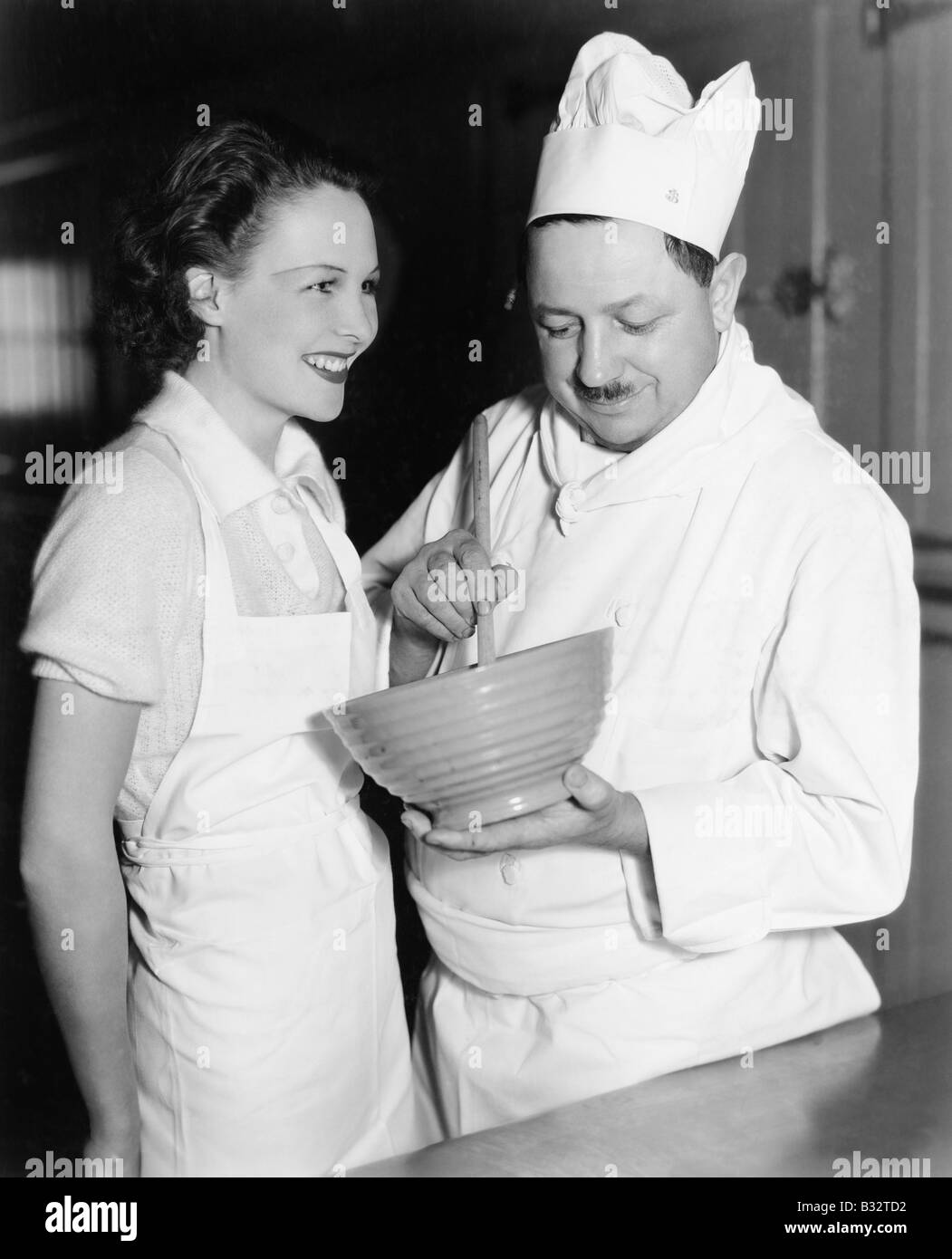 Profilo di uno chef di agitazione una miscela in una ciotola e una giovane donna in piedi accanto a lui Foto Stock