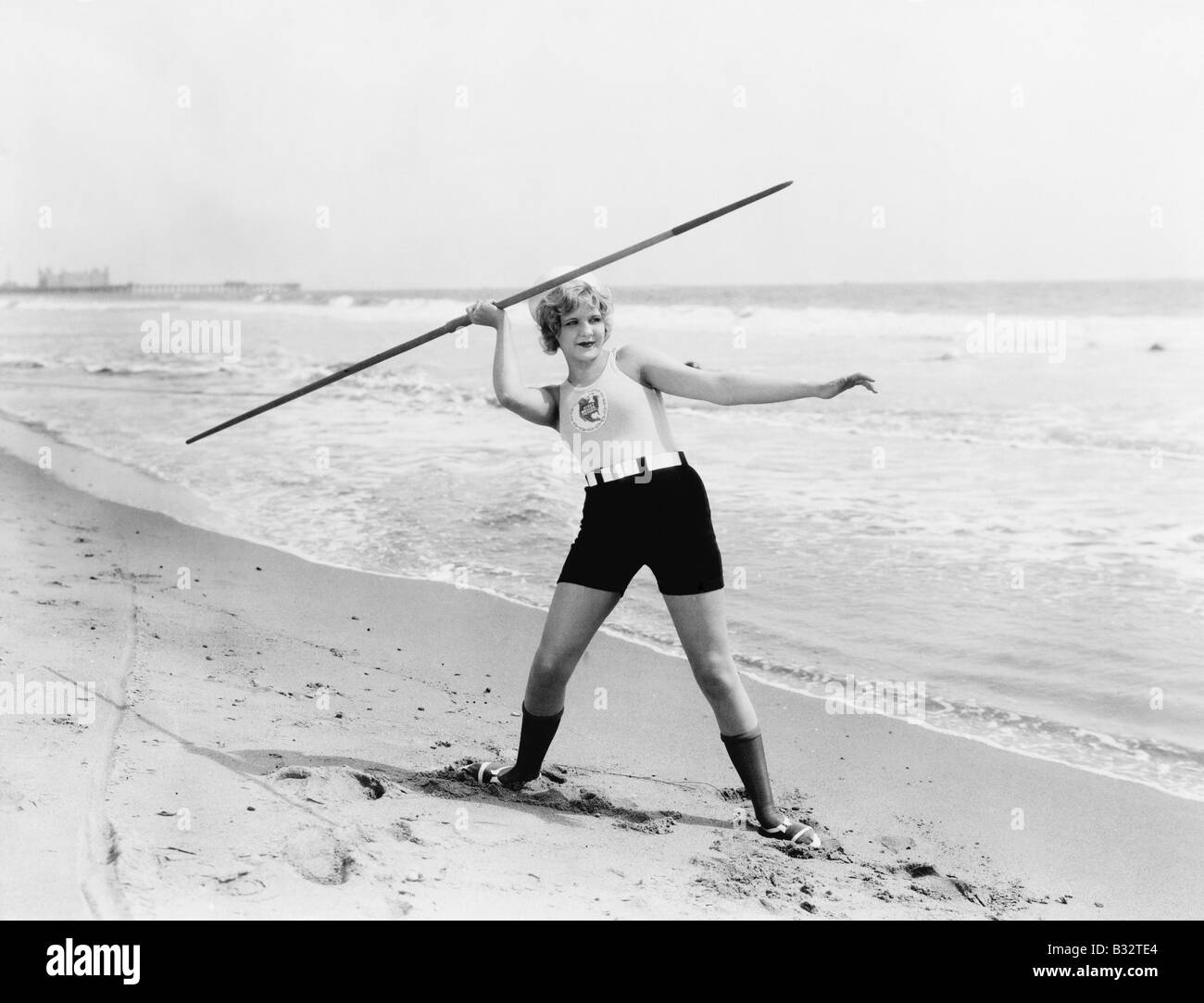 Giovane donna si prepara a lanciare un giavellotto sulla spiaggia Foto Stock