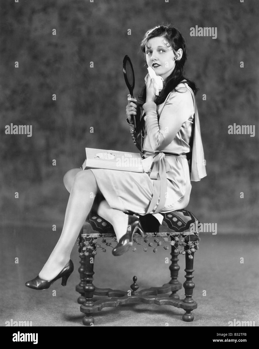 Giovane donna seduta su uno sgabello tenendo un specchietto di cortesia Foto Stock