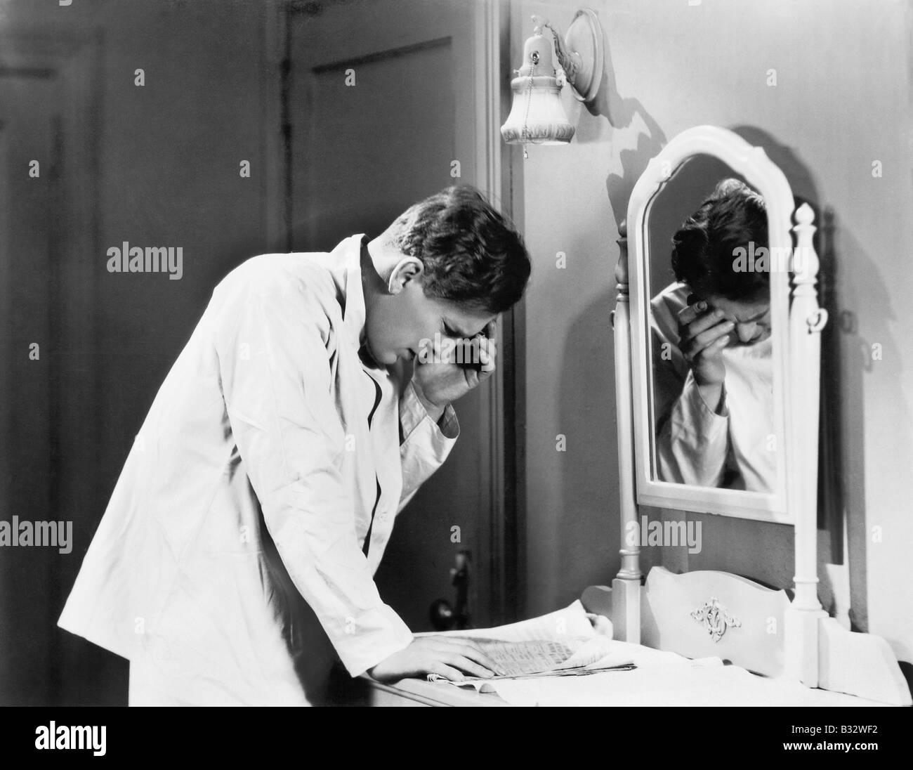 L'uomo la piegatura su un pezzo di carta sul suo comò e tenendo la sua testa Foto Stock
