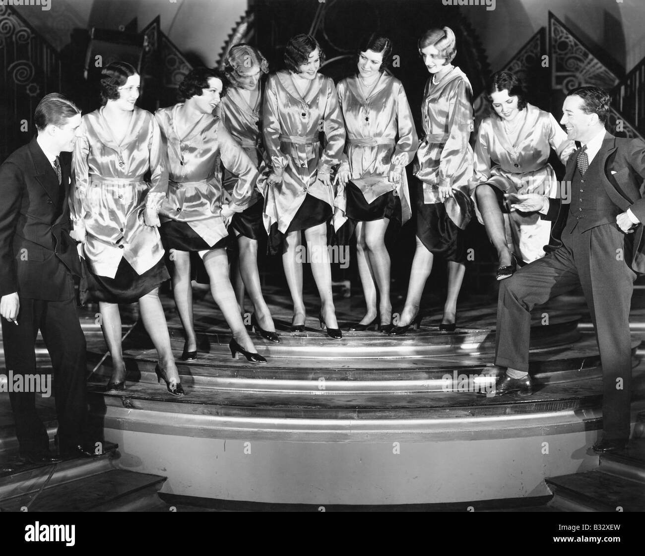 Un chorus line di donne in mostra le loro gambe per due uomini Foto Stock