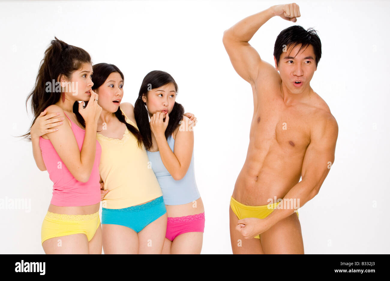 Tre giovani donne sguardo scioccato come un uomo muscolare colpisce alcune pose per impressionarli Foto Stock