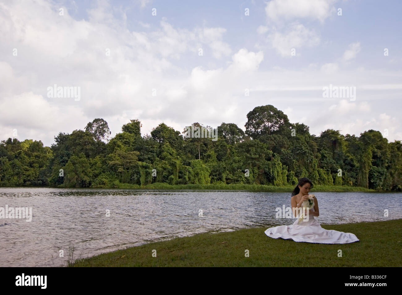 Una bella donna asiatica si siede al fianco di un lago a Singapore nel suo abito da sposa Foto Stock