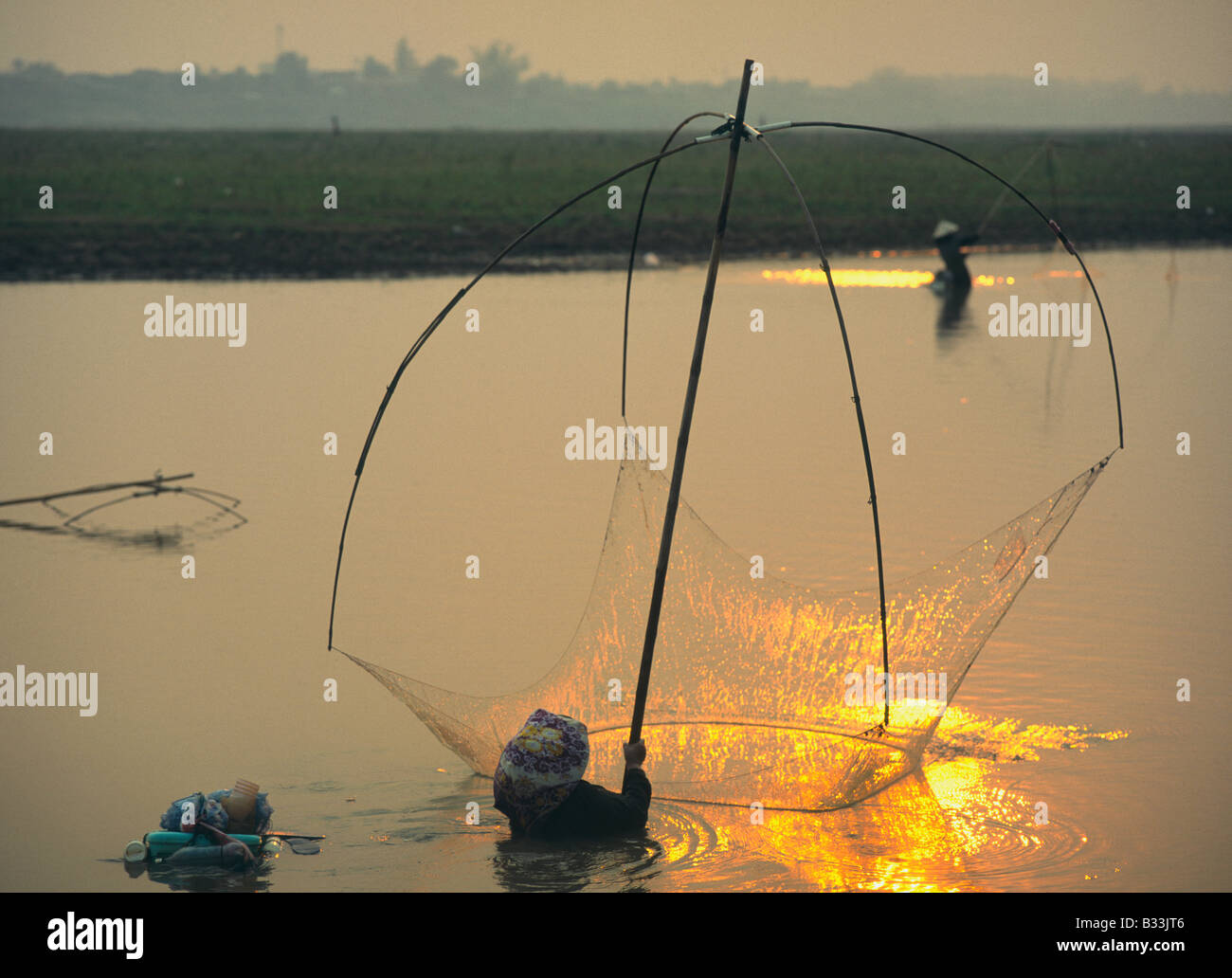 Laos Ventiane fiume Mekong donne la pesca con luce reti da pesca su una canna da pesca in piedi in acqua al tramonto Foto Stock