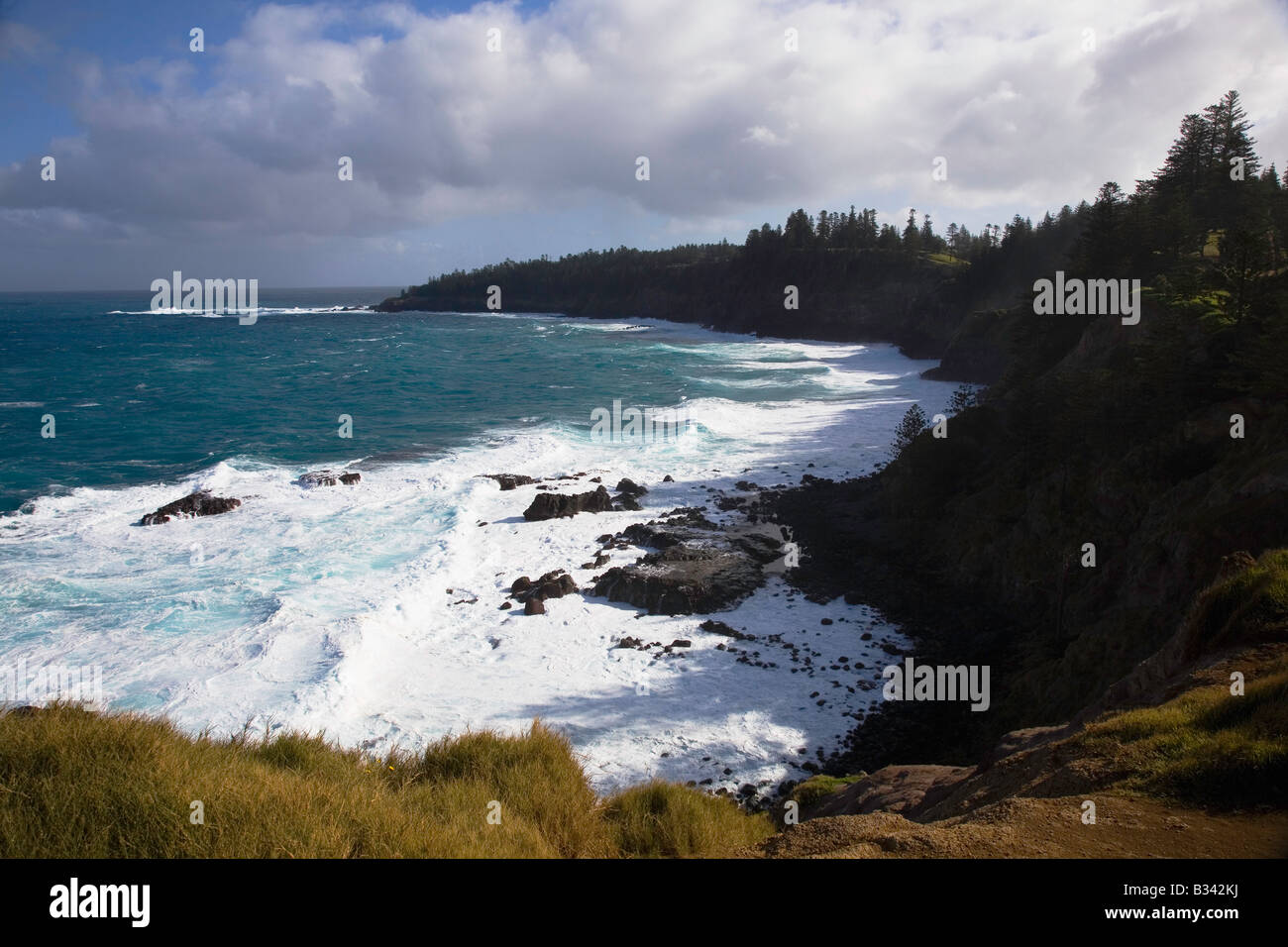 Vista della Cresswell Bay e della sua spettacolare costa con le onde che si infrangono contro le rocce con il sole che splende e la nuvola rotta, Norfolk Island, Australia Foto Stock