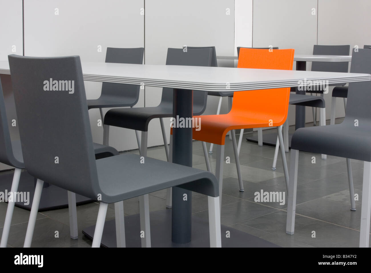 Sedia arancione tra sedie grigio Foto Stock