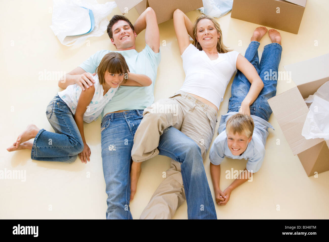 Famiglia sdraiato sul pavimento da scatole aperte nella nuova casa sorridente Foto Stock