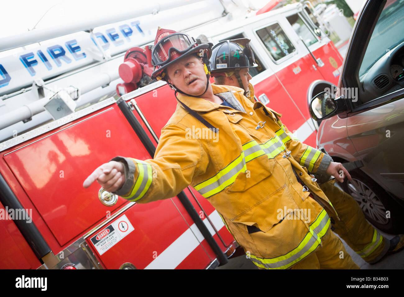 Fireman rivolti a qualcosa con un altro pompiere utilizzando le ganasce della vita sulla portiera di una macchina Foto Stock