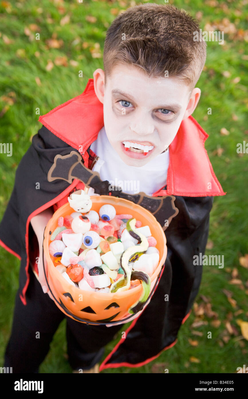 Ragazzo giovane all'aperto indossando il costume del vampiro in azienda di Halloween Candy Foto Stock