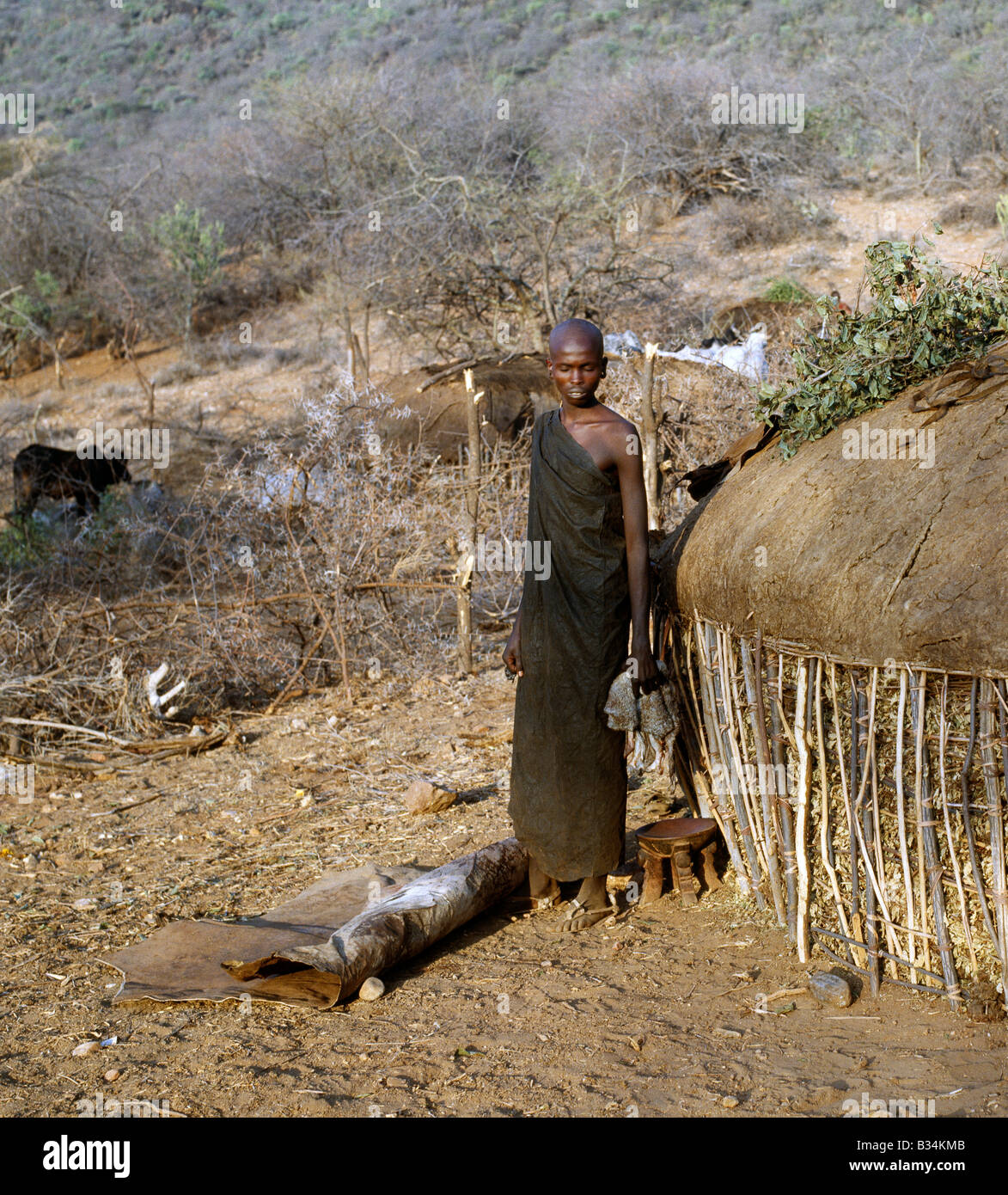 Kenya, Samburu District, South Horr. Un Samburu gioventù nella circoncisione abbigliamento pensively attende al di fuori di sua madre casa per il suo turno " sotto il coltello". Il circumciser inizia ad operare sui figli dei più alti prima di famiglia e si muove velocemente in un senso orario directionBoys non sono ammessi per mostrare alcun segno di paura o dolore. Anche il lampeggio di una palpebra è disapprovato. Foto Stock