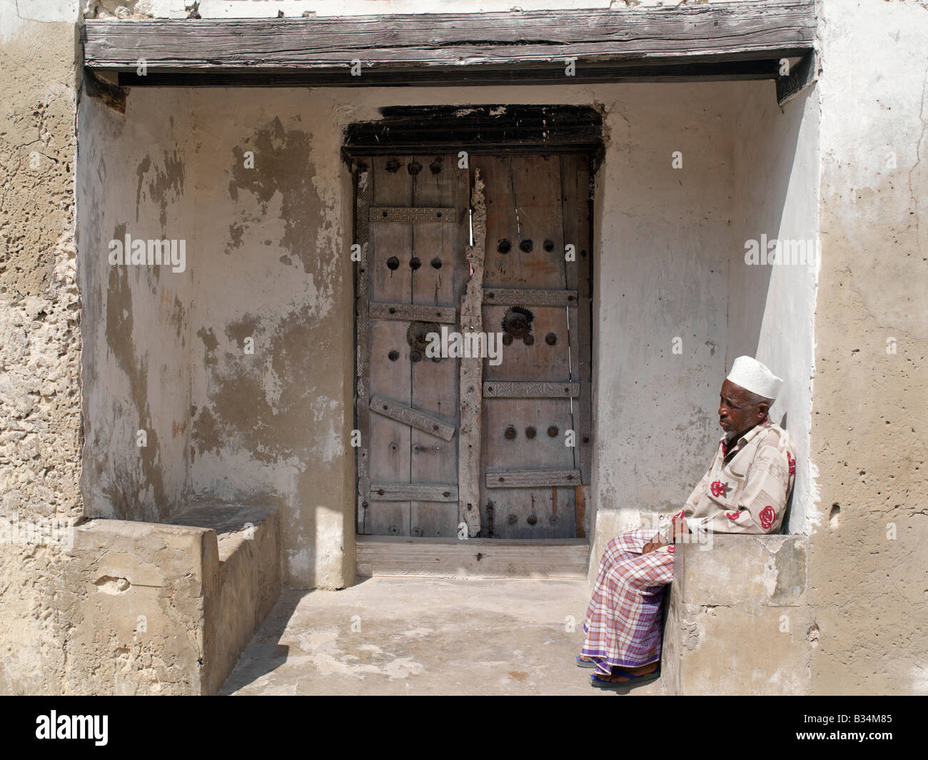 Kenya, Pate Island, Faza. Un uomo in swahili si siede su una panca in  pietra all'ingresso del composto di una grande casa vecchia con una  massiccia trave e decorate con ante in