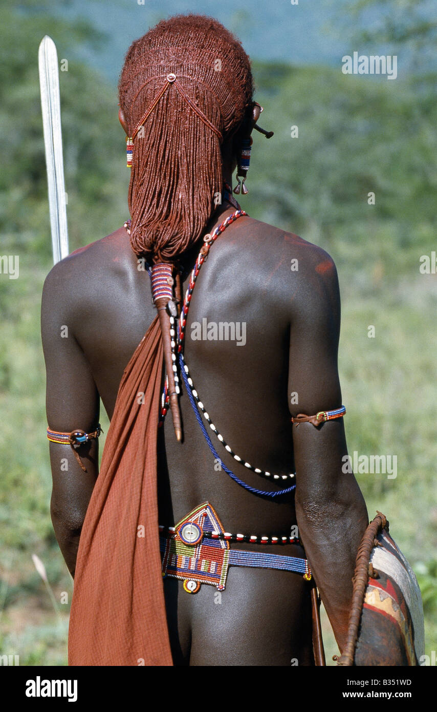 Kenya, Kajiado, Ilbisil. Una vista posteriore di un guerriero Masai che risplende con lunghe trecce ochred legato in una spiralina. Questo singolare acconciatura lo contraddistingue da altri membri della sua società. La sua cintura di perline è di un solo stile indossata da guerrieri. Il po' di rame a forma di campana ornamento orecchie pendenti dal suo allungate e decorate lobo è anche peculiari per il Maasai. Foto Stock