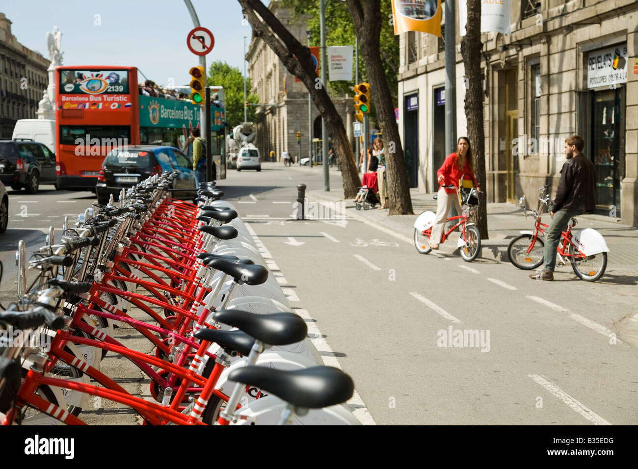 Spagna Barcellona fila di Bicing noleggio biciclette sul marciapiede giovane con le biciclette a noleggio e double decker bus turistici Foto Stock