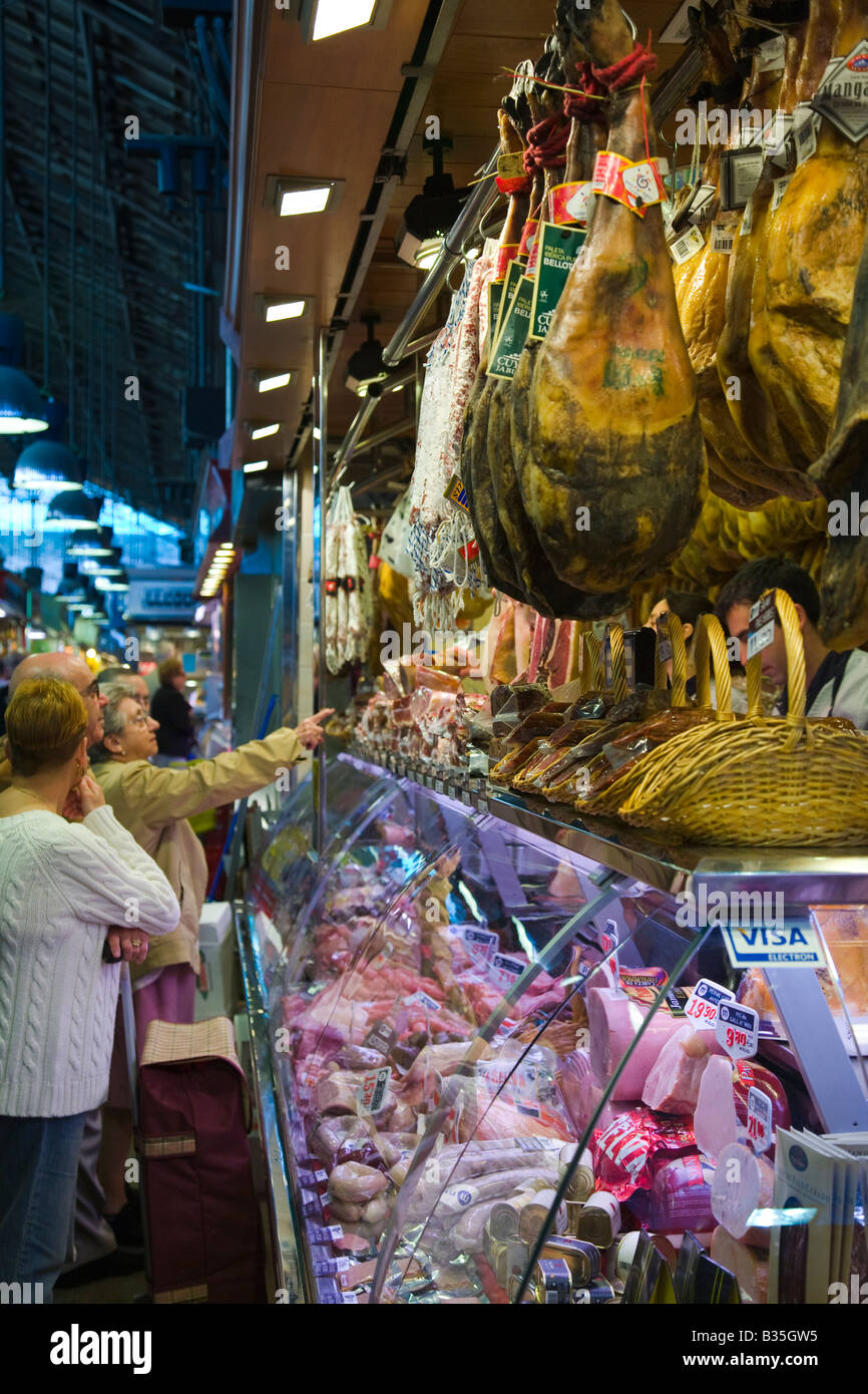 Spagna Barcellona supporto clienti al negozio di macellaio in La Boqueria produrre prosciutto di mercato garretti appendere sul display Foto Stock