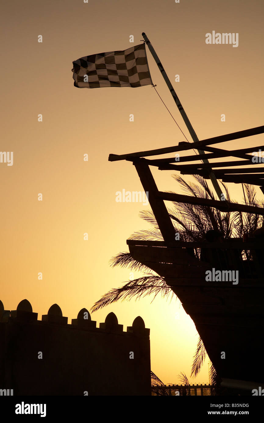 Bandiera a scacchi battenti sulla barca dhow al 2007 Bahrain Grand Prix di Formula 1 con il tramonto Palm tree e il castello arabo fort Foto Stock
