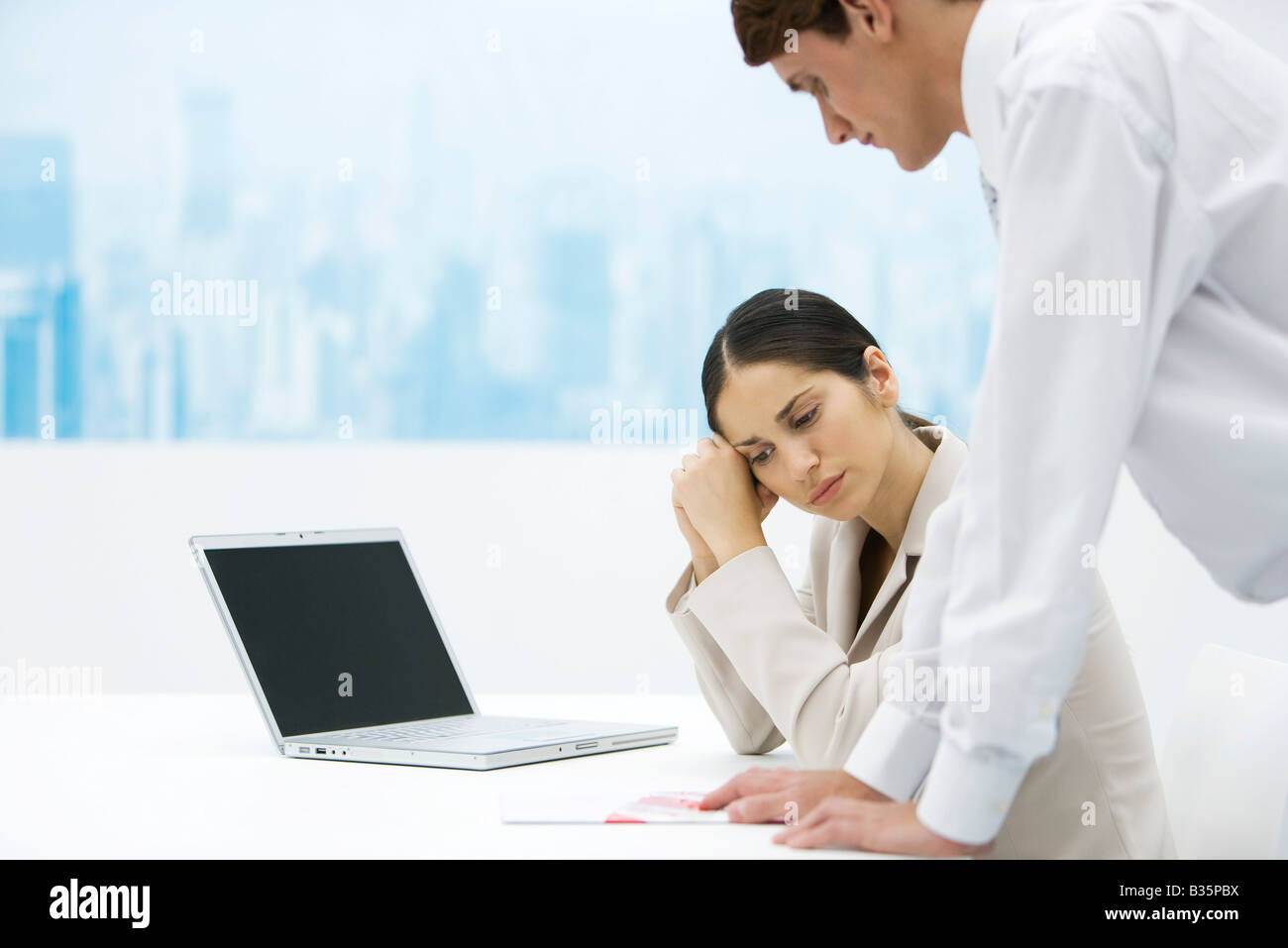 Donna che guarda verso il basso e tenendo la testa, collega appoggiato sulla scrivania e guardando sopra la sua spalla Foto Stock