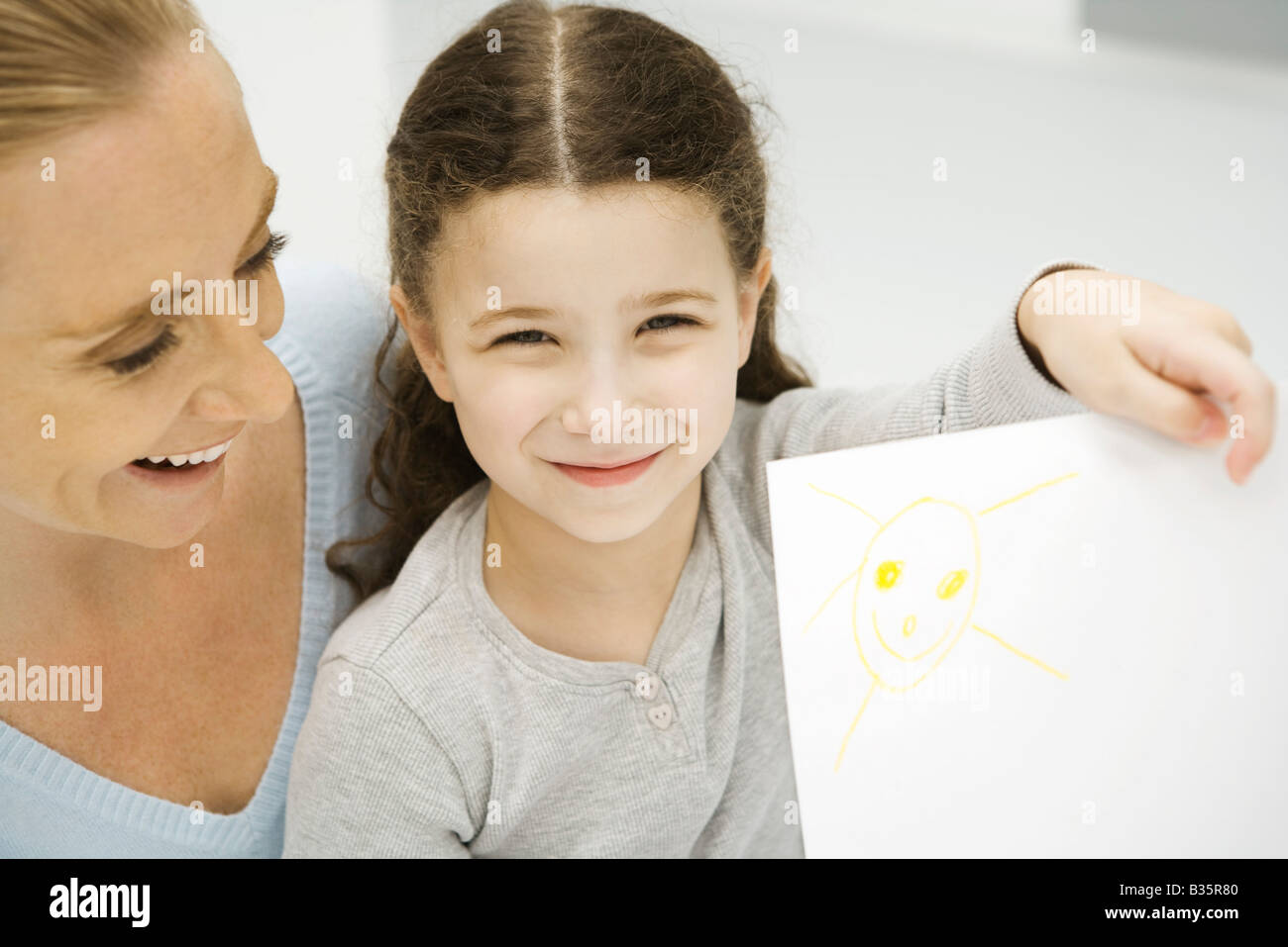 Ragazza con fino e che mostra il disegno del sole, madre sorridente dietro la figlia Foto Stock