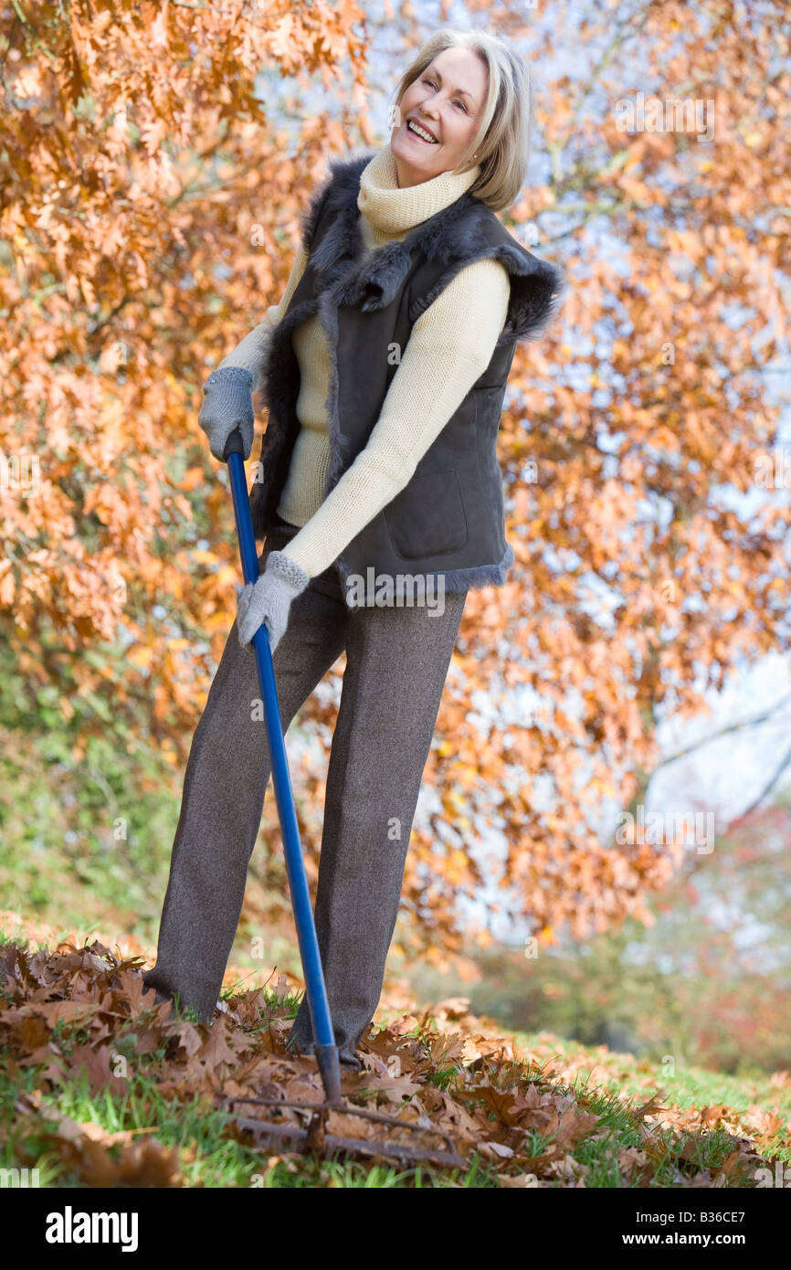 Donna all'aperto a rastrellare foglie e sorridente (messa a fuoco selettiva) Foto Stock