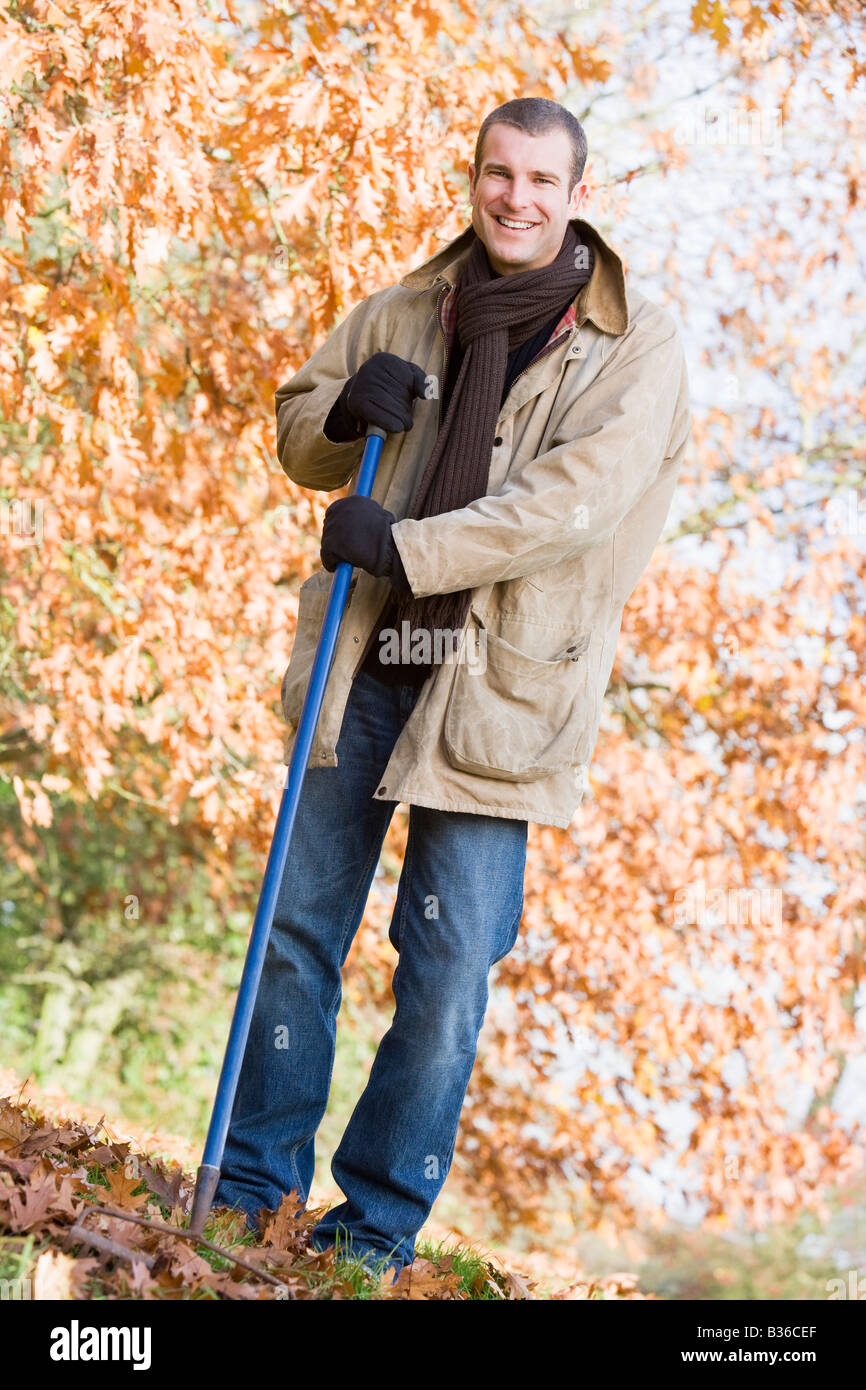 L'uomo all'aperto a rastrellare foglie e sorridente (messa a fuoco selettiva) Foto Stock