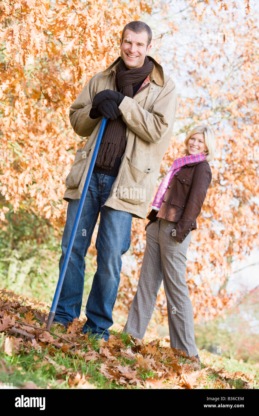 L'uomo all'aperto a rastrellare foglie e donna sorridente di sfondo (il fuoco selettivo) Foto Stock